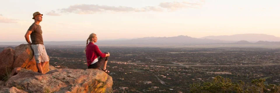 Two hikers enjoy the panoramic view of the rugged landscape from a high elevation at dusk.