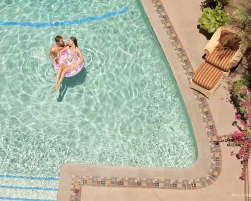 A happy couple enjoys the clear water while floating on an inflatable tube in the beautiful, mosaic-trimmed outdoor.
