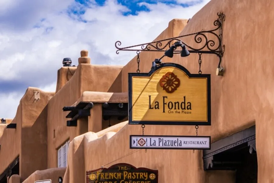 A beautiful adobe facade displays the ornate hanging signs for the hotel and downtown Santa Fe restaurants.