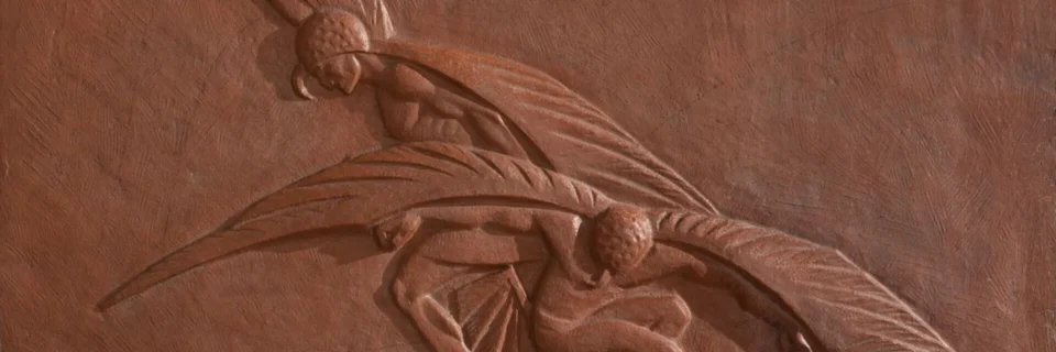The textured wall features an intricate terracotta relief depicting two stylized, winged figures.