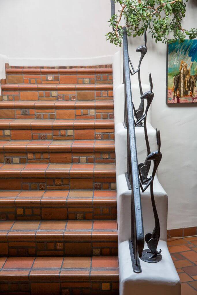 The colorful tiled staircase features a unique, custom wrought iron railing designed with stylized animal sculptures.