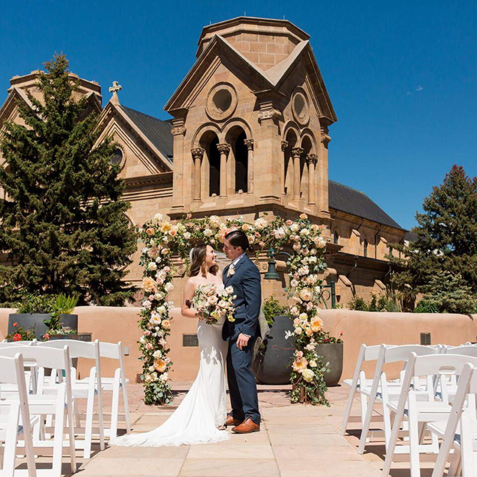 The newly married couple poses under a rose arch at a beautiful outdoor wedding venue.