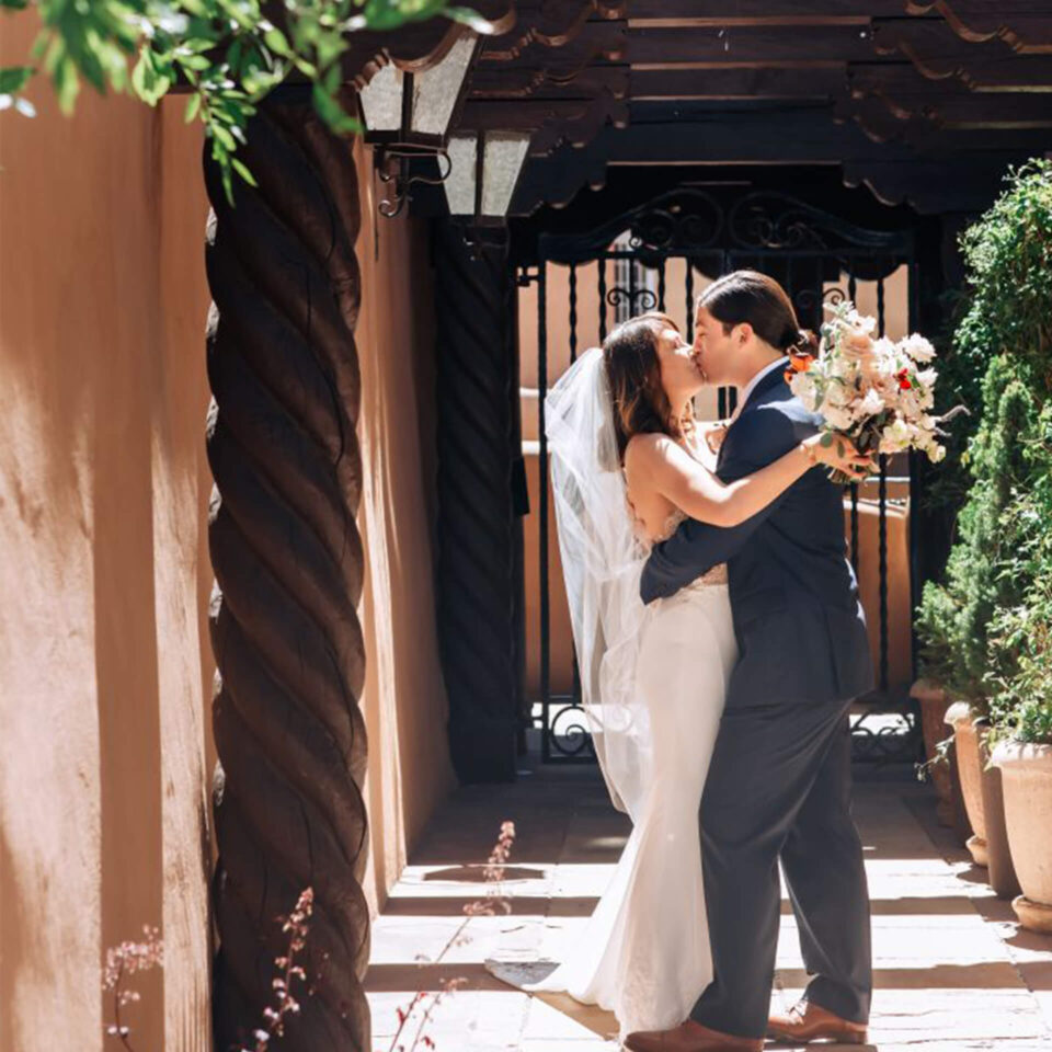 A newly married couple shares a tender kiss under a carved wooden archway at a beautiful Santa Fe wedding venue.