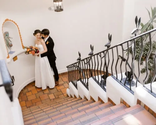 A bride and groom embrace on a tiled staircase landing decorated with unique rabbit-themed railings.