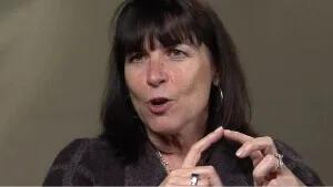 Close-up portrait of a woman with bangs talking passionately and emphasizing a point with her hands.
