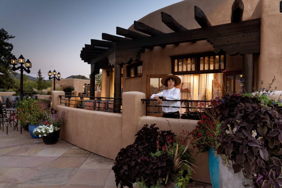 A woman leans on a railing holding wine on a beautiful Southwestern-style outdoor patio at twilight.
