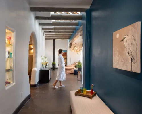 A guest in a white robe walks down the tranquil spa hallway decorated with Southwest architecture.