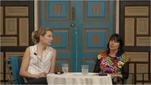 Two women are seated for a panel discussion in a richly decorated event setting with a vibrant blue door backdrop.