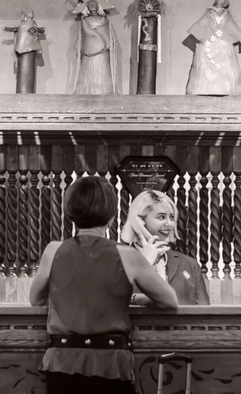 A smiling hotel employee assists a guest at the ornate front desk beneath cultural statues.