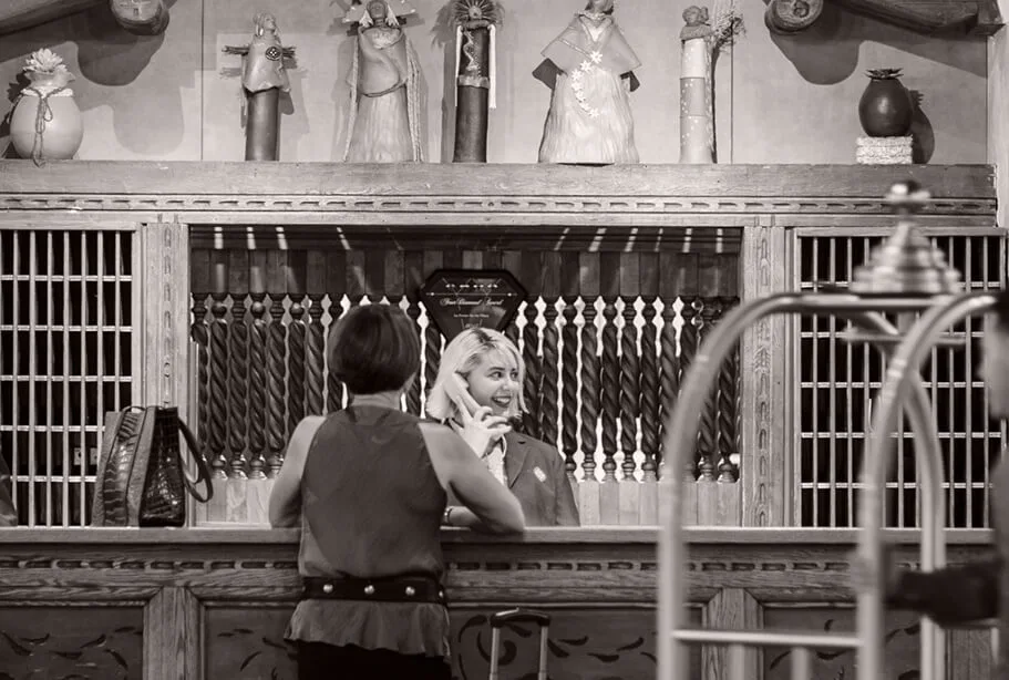 A welcoming staff member assists a guest checking in at the finely carved wooden front desk.