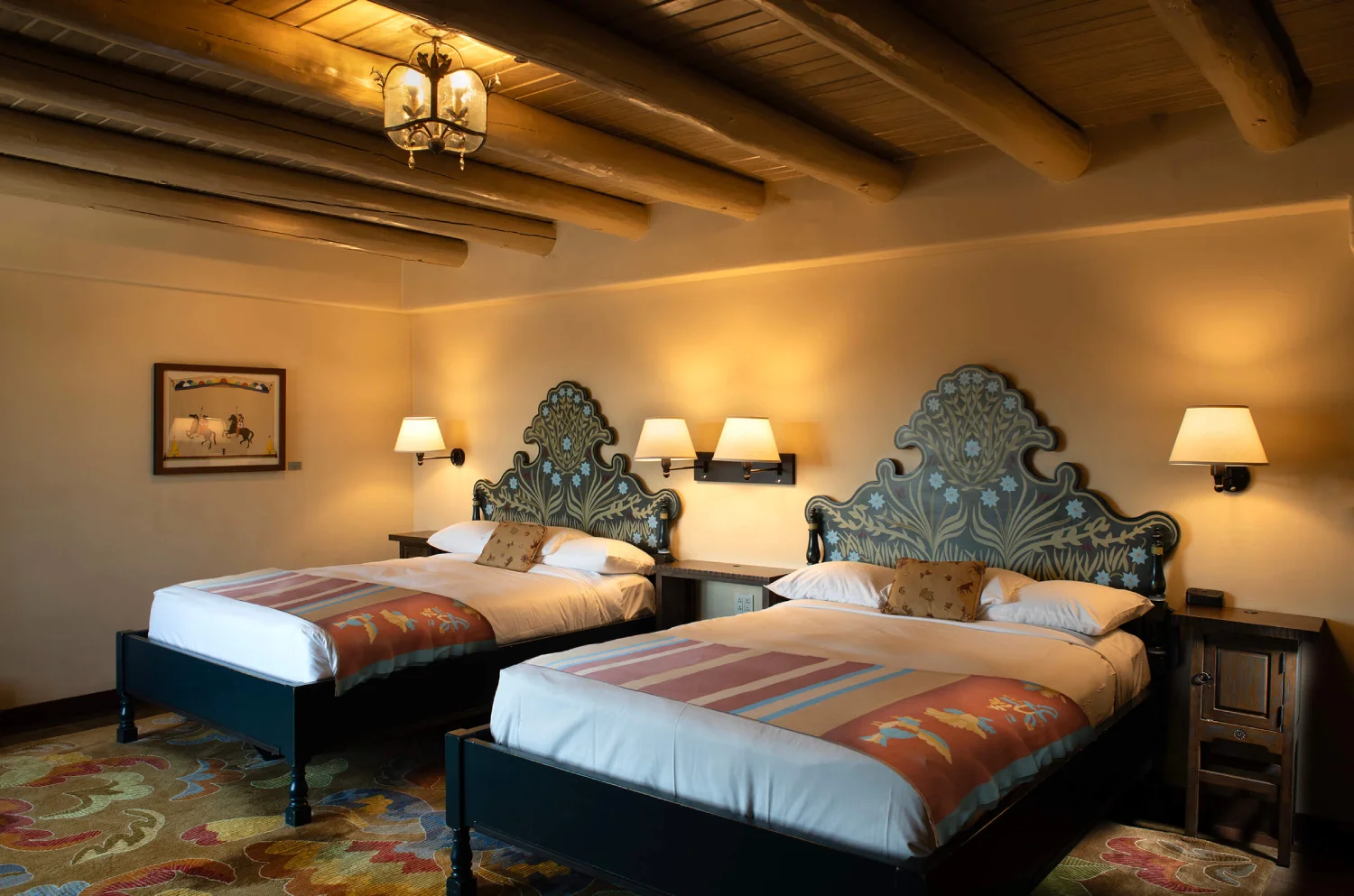 The cozy, traditionally styled guest room features two queen beds and a rustic viga beam ceiling.