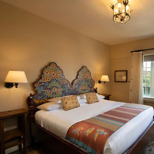 A king bed with a colorful woven runner and an artistic painted headboard defines this inviting boutique hotel room.