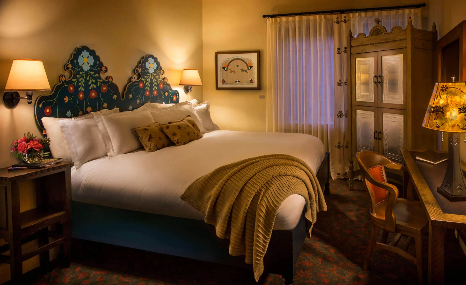 A luxurious santa fe hotel room showcasing a painted floral headboard and traditional carved wooden furniture.