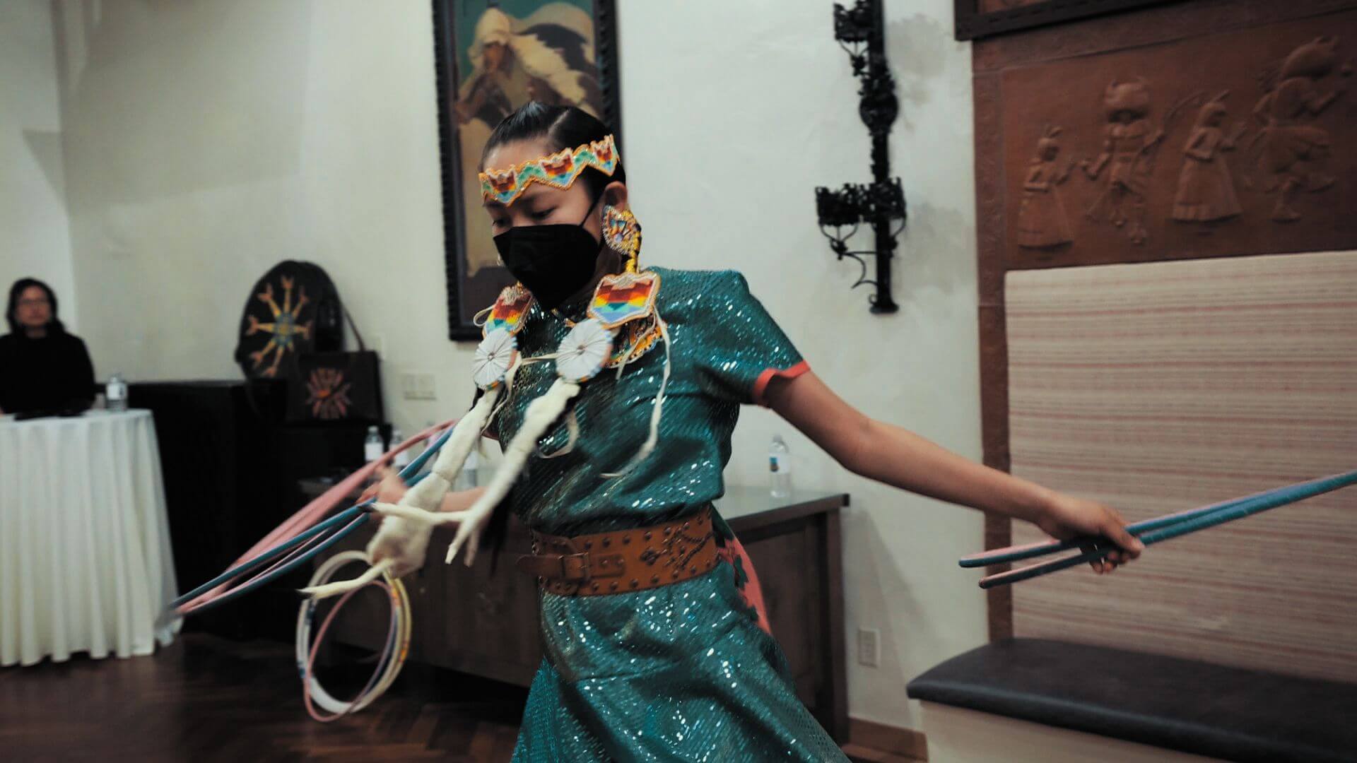 A dancer in traditional regalia and a mask performs a hoop dance in the elegant interior event space.