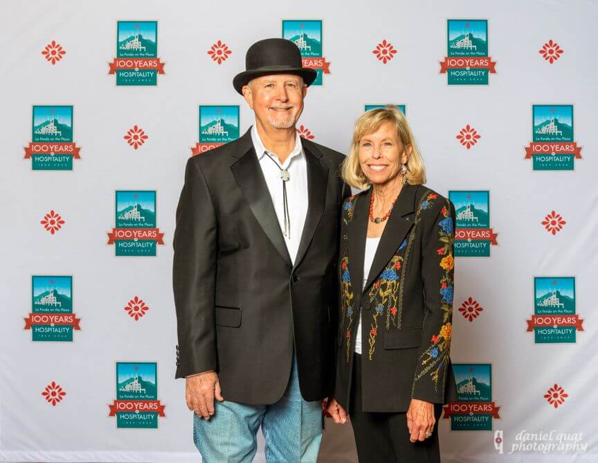 Two guests pose in formal wear against the repeating logo backdrop for the special event.