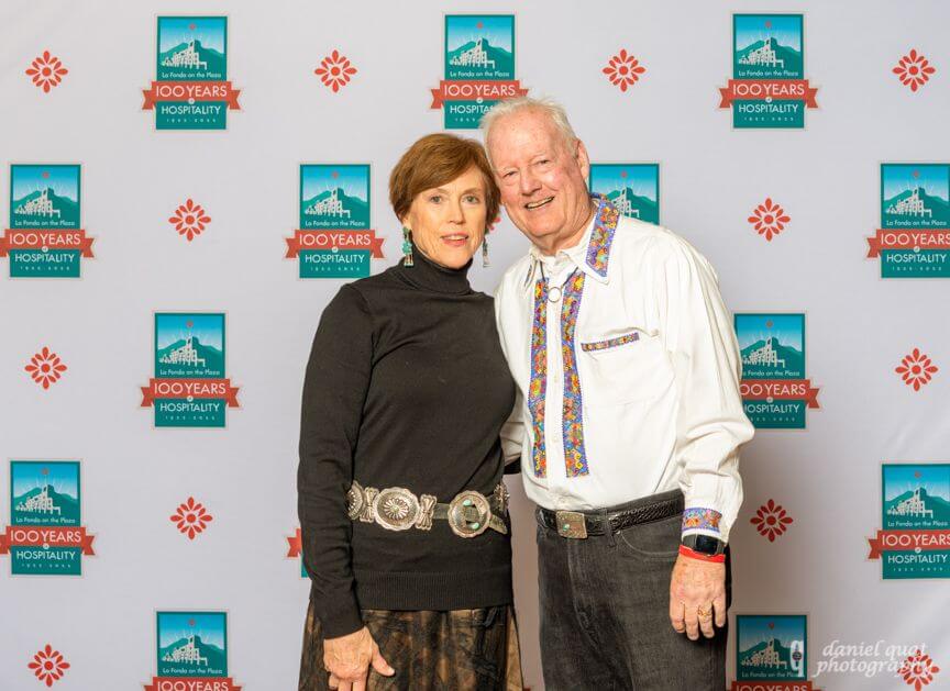 A couple in Southwestern attire poses and smiles against a branded event spaces backdrop.
