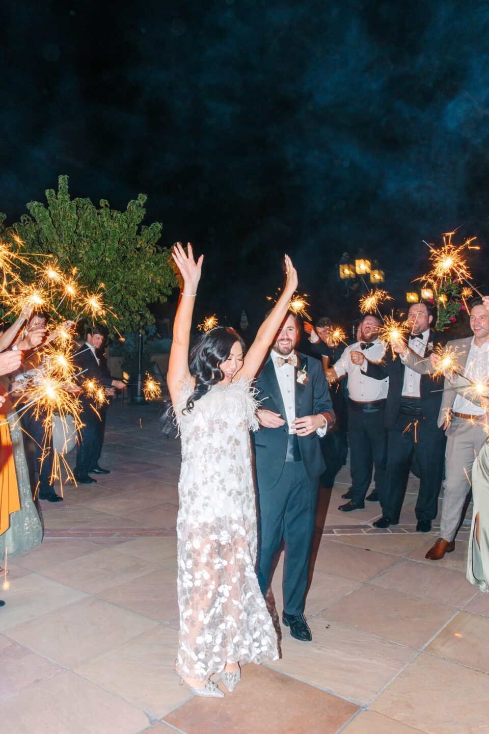 A newly married couple exits their reception, surrounded by guests holding sparklers at the event spaces.