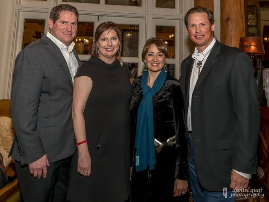 Four smiling, formally dressed guests stand together inside the beautifully decorated event spaces.