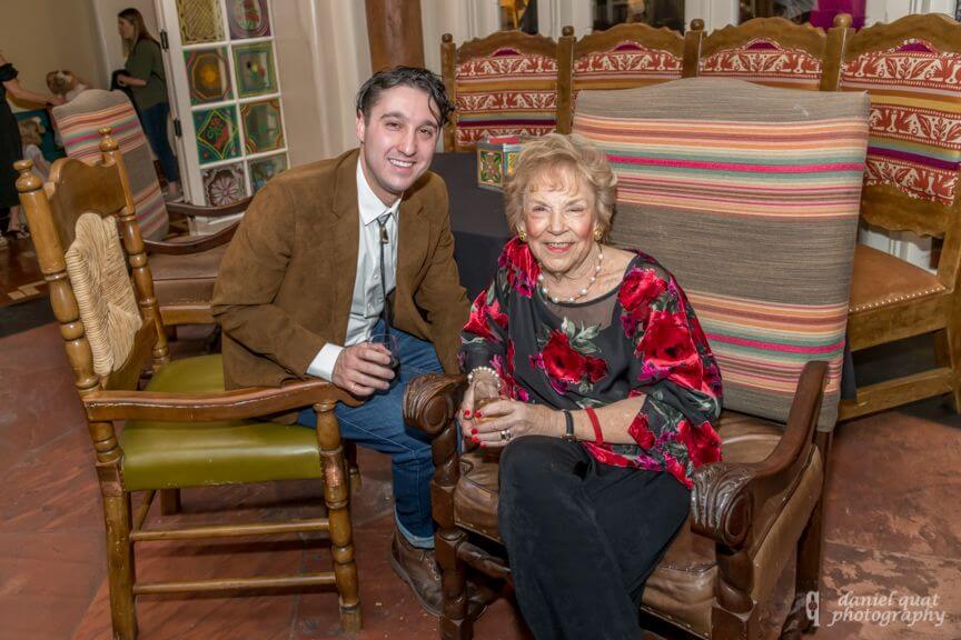 A smiling man and woman sit in rustic wooden chairs enjoying a social event inside one of the banquet halls.