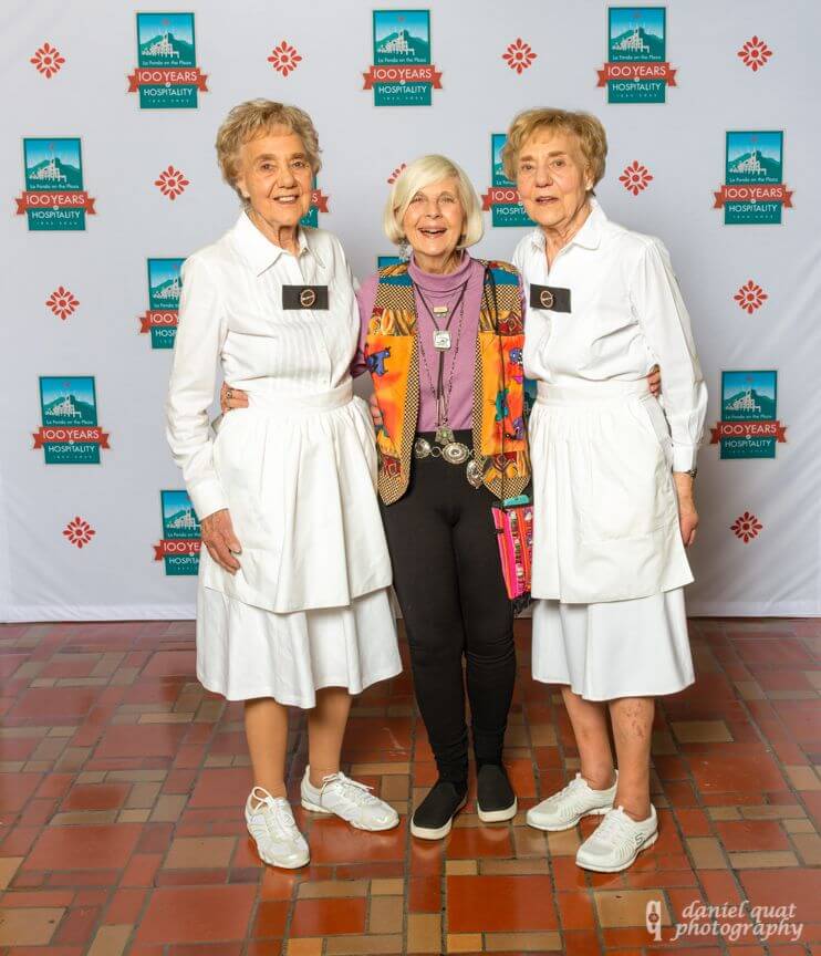 Three smiling associates stand in front of a branded centennial backdrop celebrating 100 years of service.