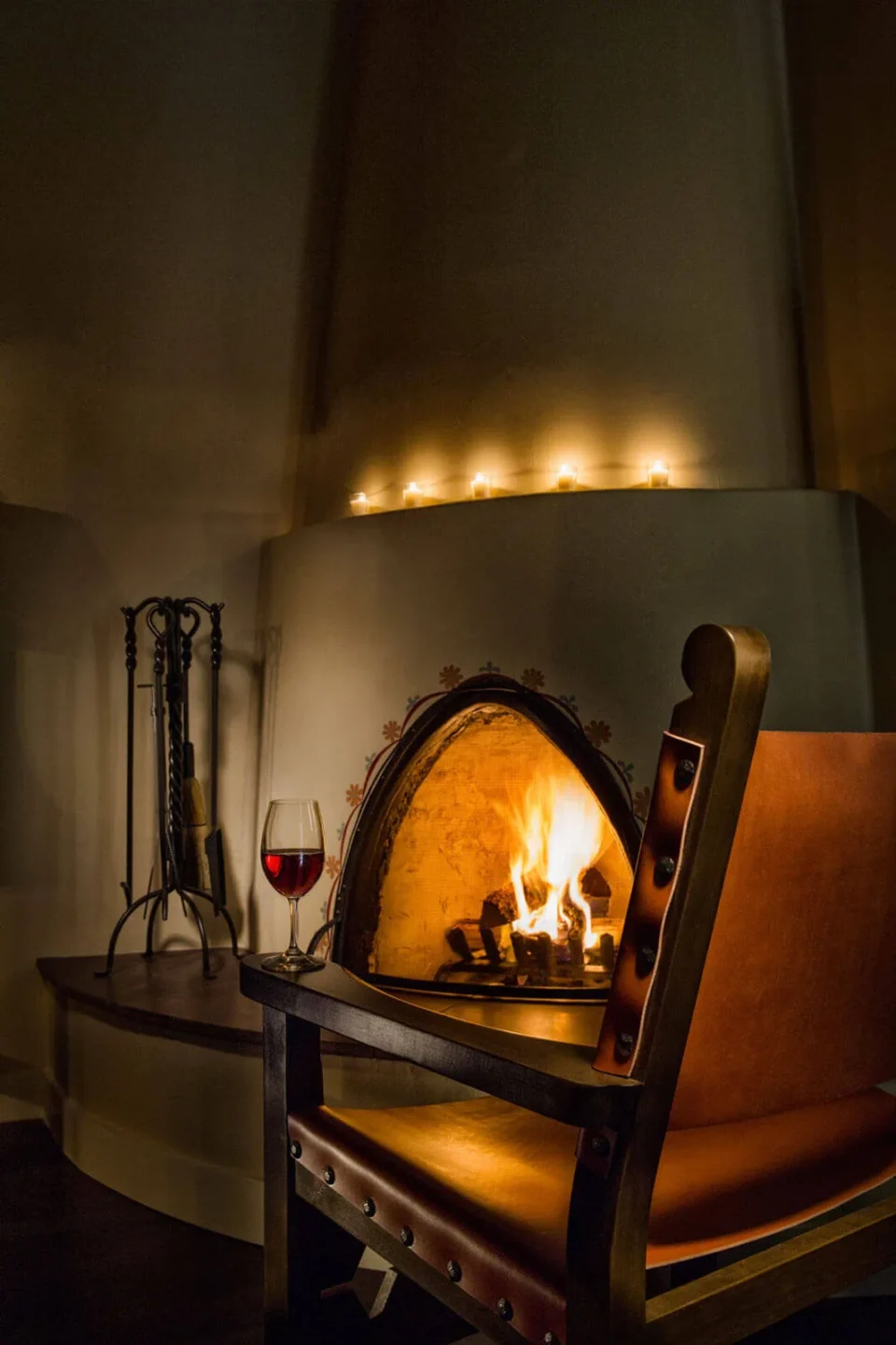 The cozy atmosphere includes a glowing kiva fireplace, a leather chair, and a wine glass, perfect for hotel suites.
