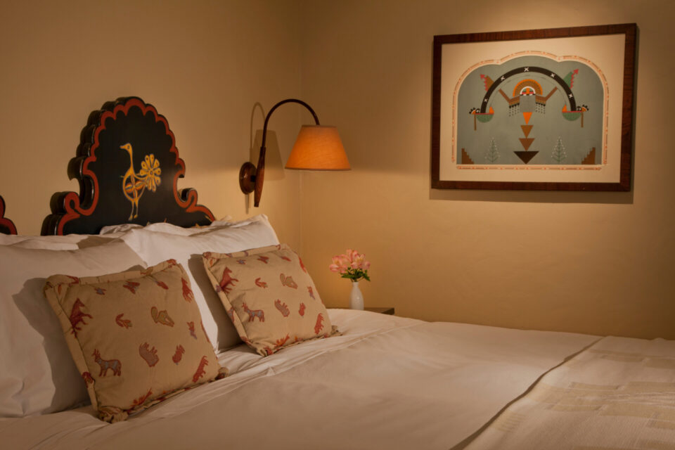 A comfortable hotel room bed detail features a painted wood headboard and unique Southwestern decor.
