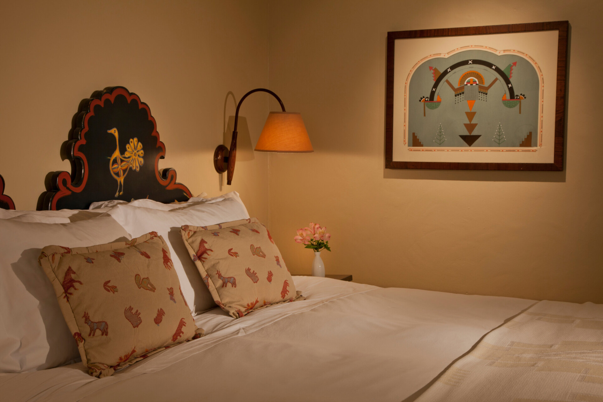 A comfortable hotel room bed detail features a painted wood headboard and unique Southwestern decor.