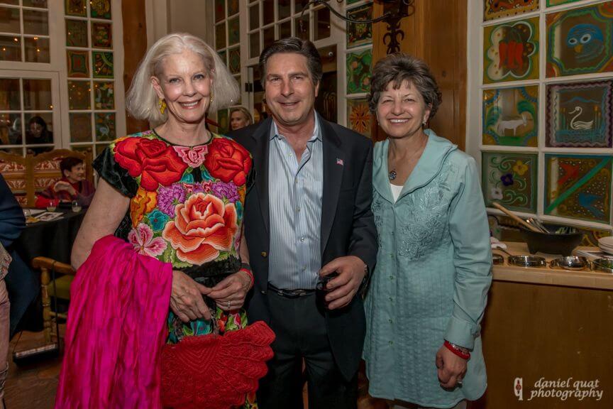 Three smiling guests stand together in a beautifully decorated event space.