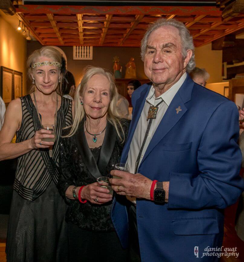 Three elegantly dressed guests pose with drinks during a beautiful banquet hall reception.