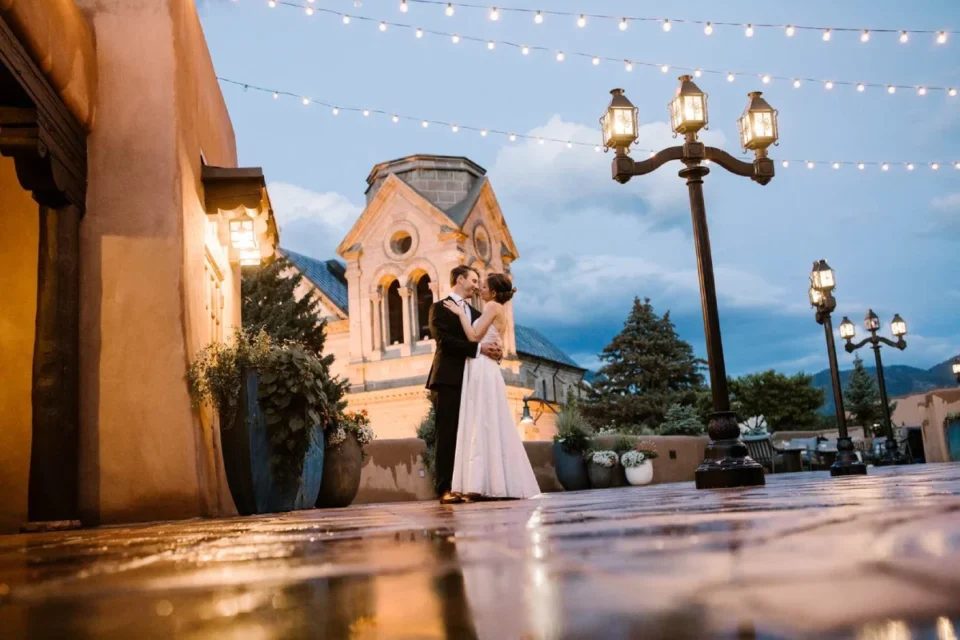 A newly married couple embraces under string lights on a historic terrace, showing a beautiful wedding venue.