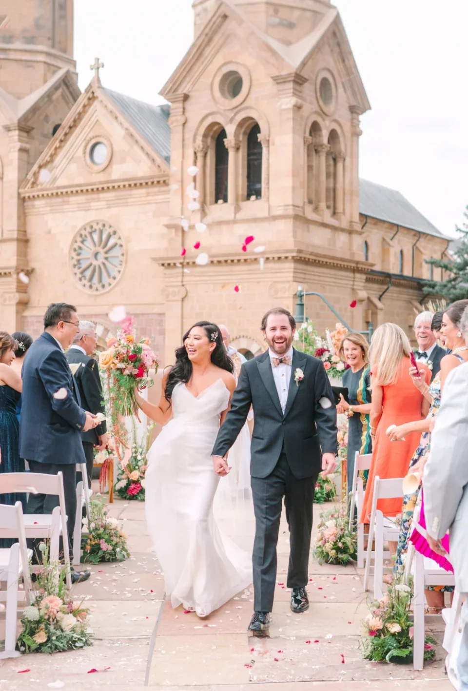 A newly married couple smiles brightly while exiting their outdoor ceremony held at a lovely wedding venue.