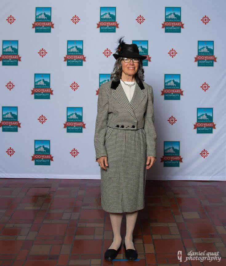 An elegantly dressed guest stands against the branded step-and-repeat banner at the hotel event spaces.