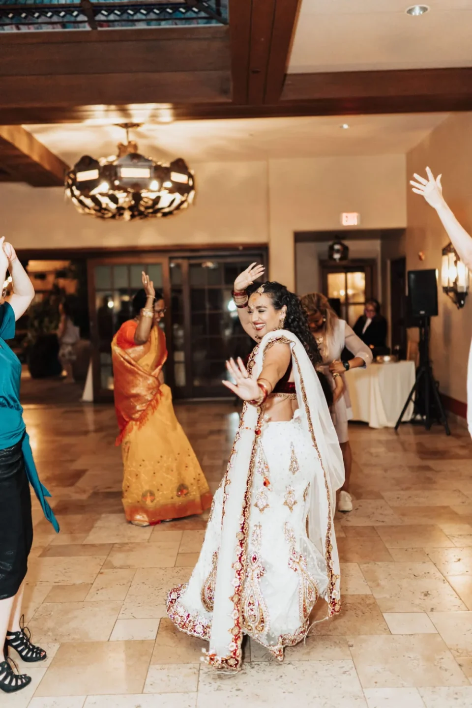 Guests in vibrant attire dance exuberantly during a wedding reception in the elegant hotel ballroom.