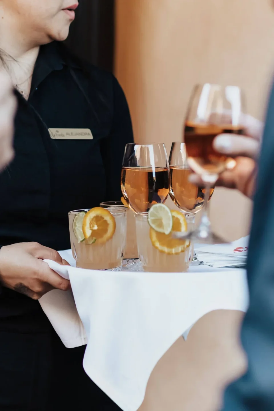 An employee delivers a tray of handcrafted cocktails and wine glasses to event attendees.