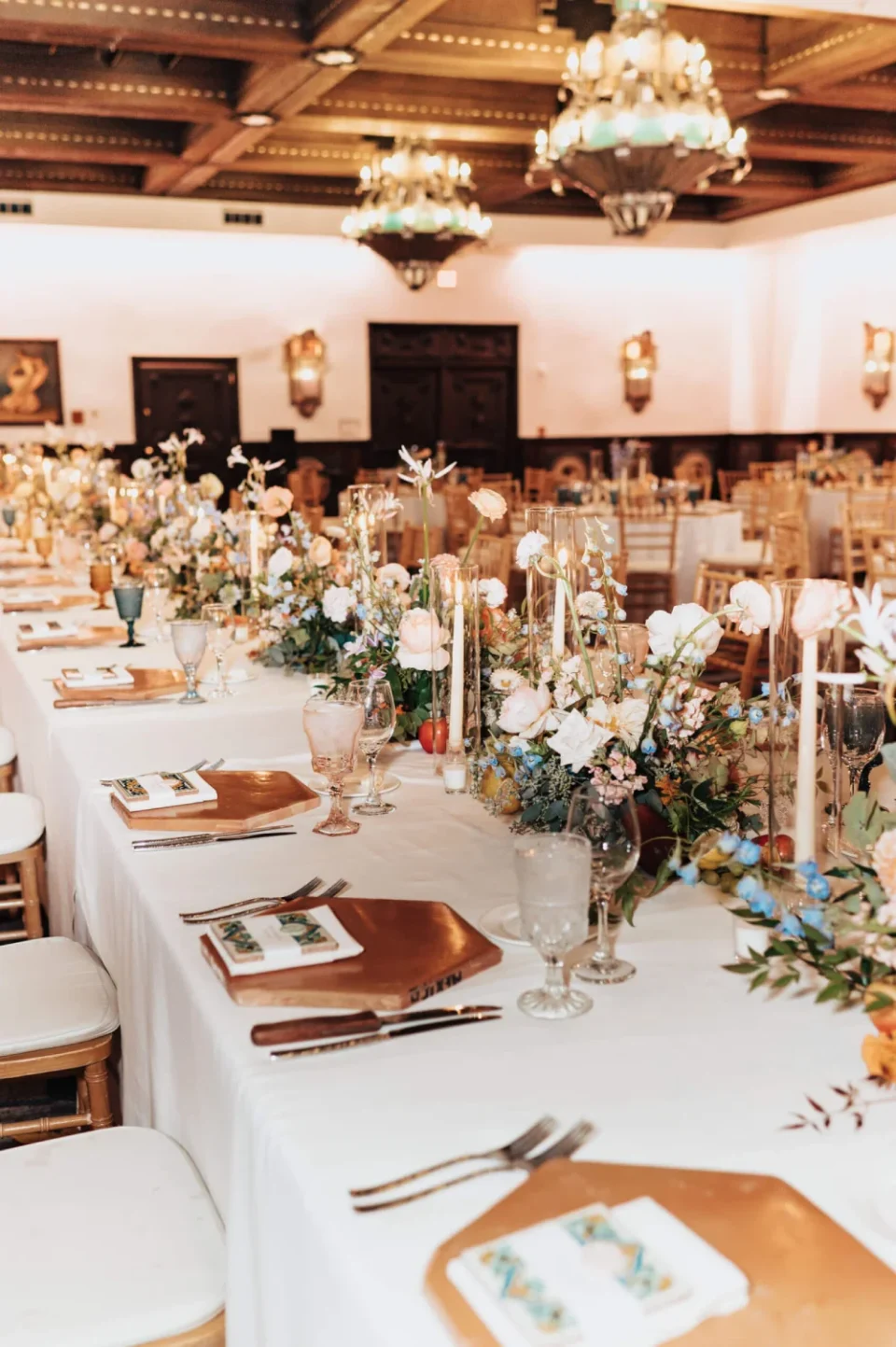 The beautifully decorated banquet hall table features lush floral arrangements, tall candles, and elegant place.