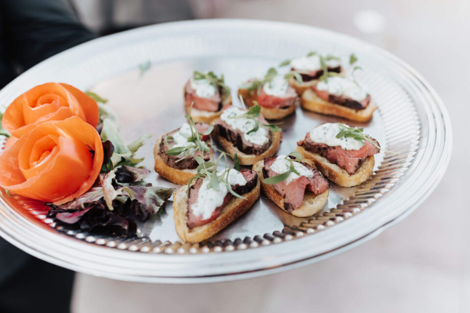 A silver platter of perfectly prepared beef crostini appetizers is displayed for an event.