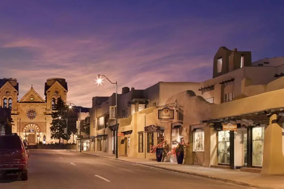 The historic adobe exterior of the boutique hotel glows next to the prominent cathedral under soft street lighting.