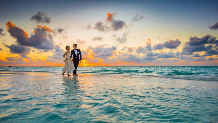 This dramatic sunset photograph captures a beautiful married couple strolling along the water's edge.