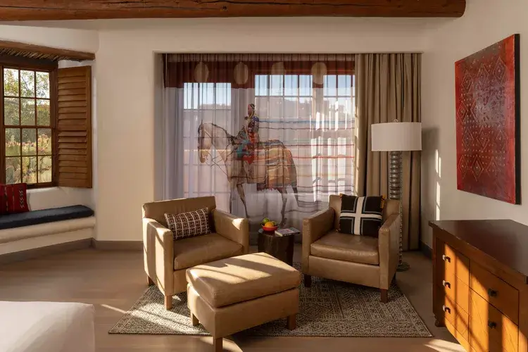A sunlit sitting area in a santa fe hotel room features cozy leather seating, rustic wooden beams, and colorful artwork.