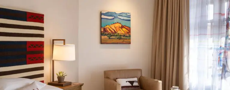 This beautiful hotel suite is decorated with Southwestern art, a patterned pillow, and a bright bedside lamp.
