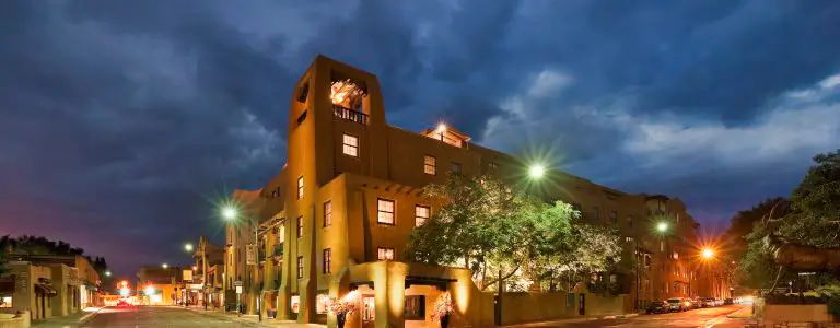 The exterior of the prominent boutique hotel features adobe architecture, warmly lit against a dramatic twilight sky.