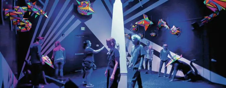 Guests mingle inside a highly stylized event space illuminated by neon blue lights and abstract geometric art.