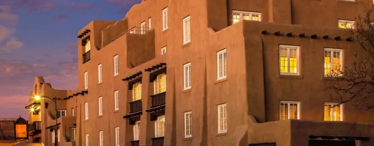 The multi-story boutique hotel features classic adobe architecture illuminated during twilight.