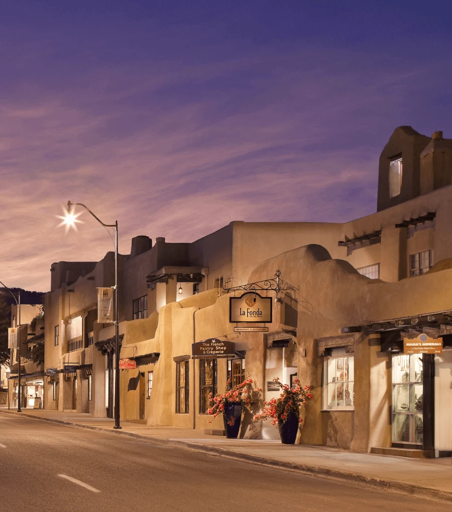 The beautiful adobe storefronts and hotels are brightly lit along the downtown street at twilight.