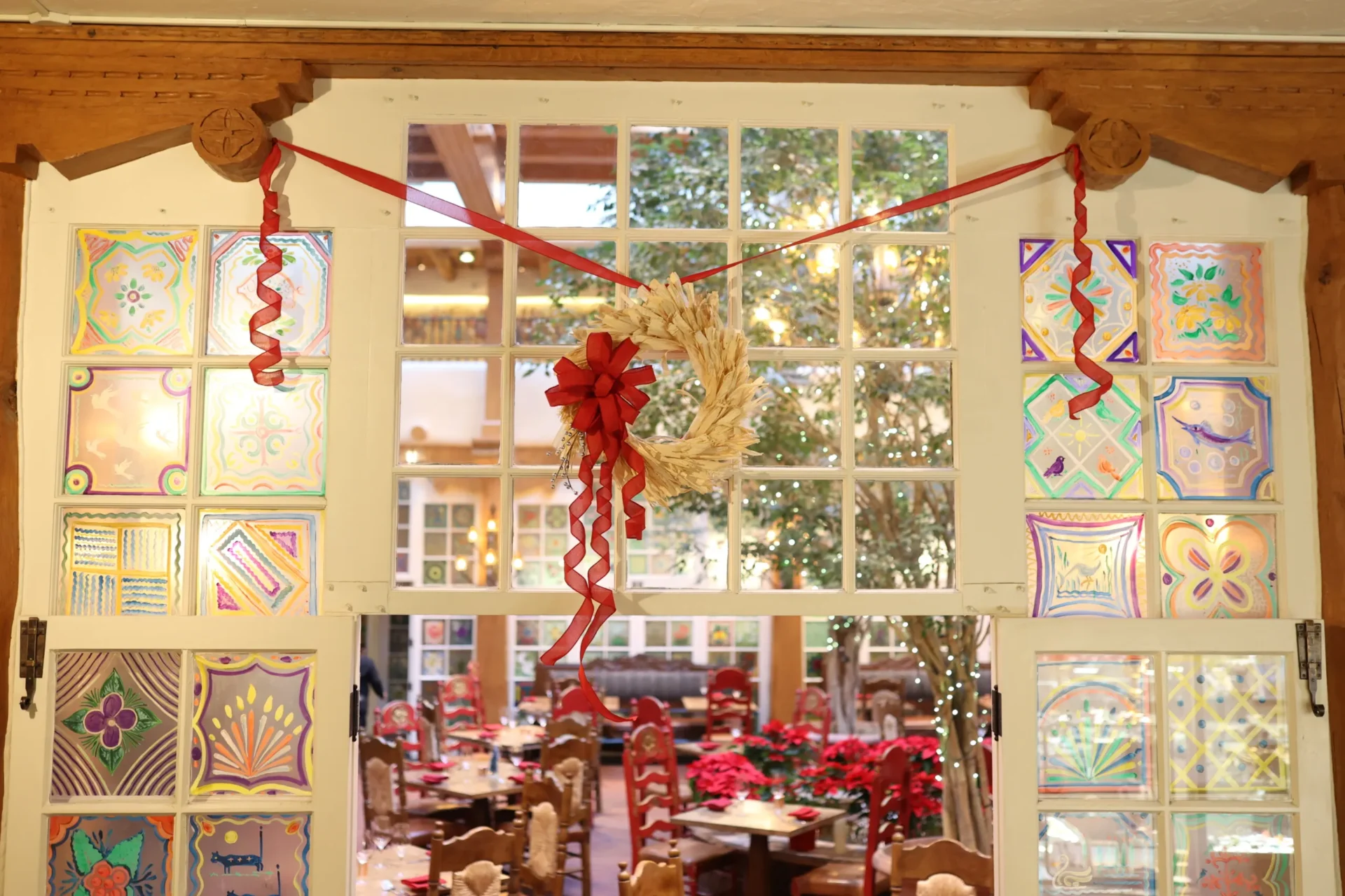 A large doorway decorated with a wreath and colorful tiles opens into a festive restaurant dining area.