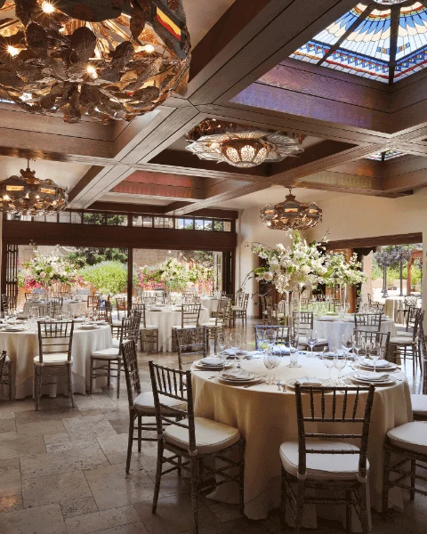 The large, elegant banquet hall is prepared for an event with formal table settings and luxurious chandeliers.
