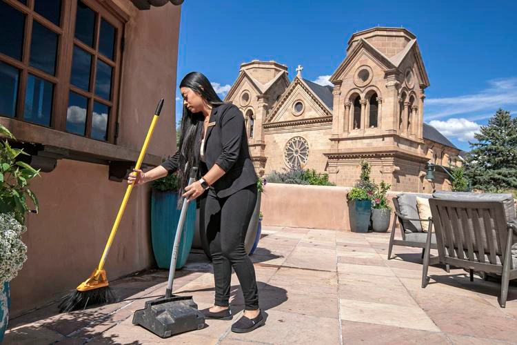 An elegantly dressed employee sweeps a tiled outdoor patio overlooking the historic church spires.
