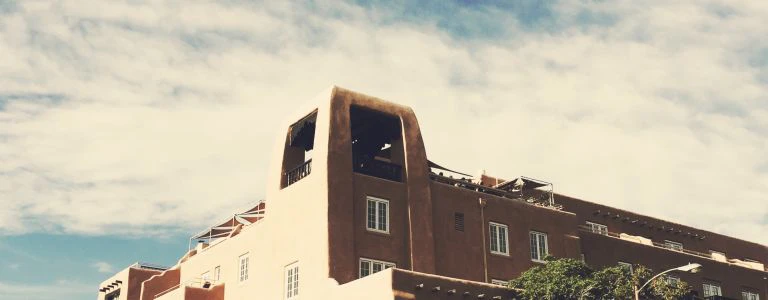 The iconic adobe exterior of the boutique hotel is seen against a bright, cloudy sky.