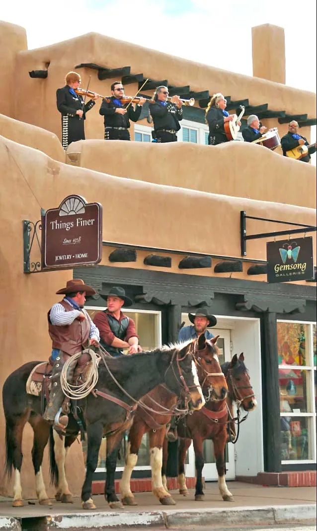 A Mariachi band plays live music on a balcony above three cowboys sitting on their horses below.