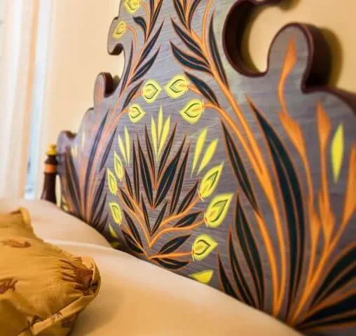 A close-up captures the colorful, hand-painted wooden headboard decoration in a luxurious hotel suite.